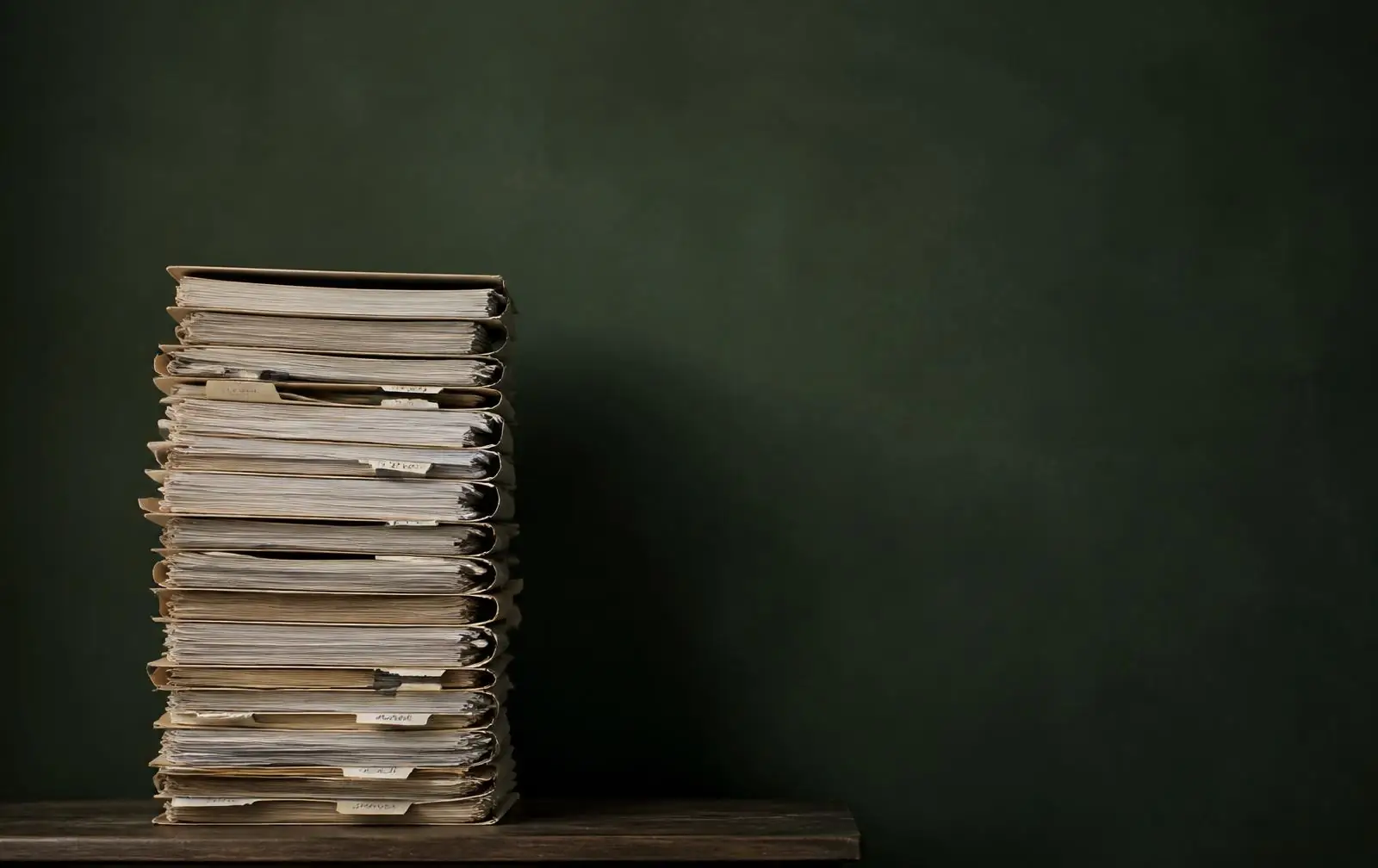 A tall stack of filed paper documents against a dark green wall