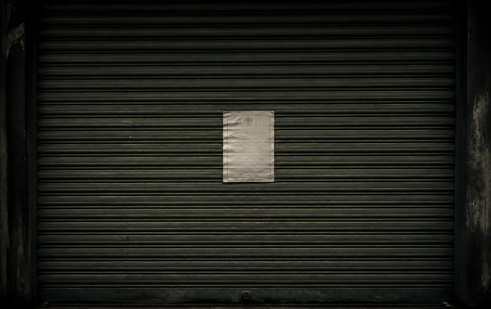 A closed metal shop shutter with an official paper notice pasted on it